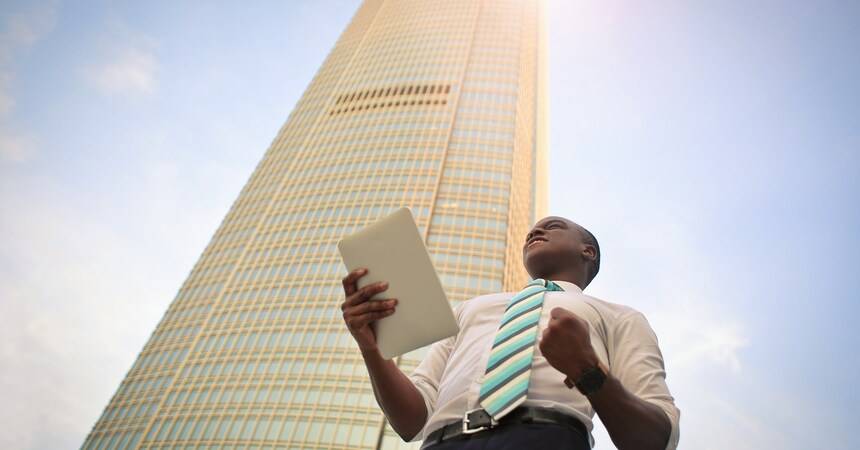 Businessman holding a tablet looking up at a tall glass office tower