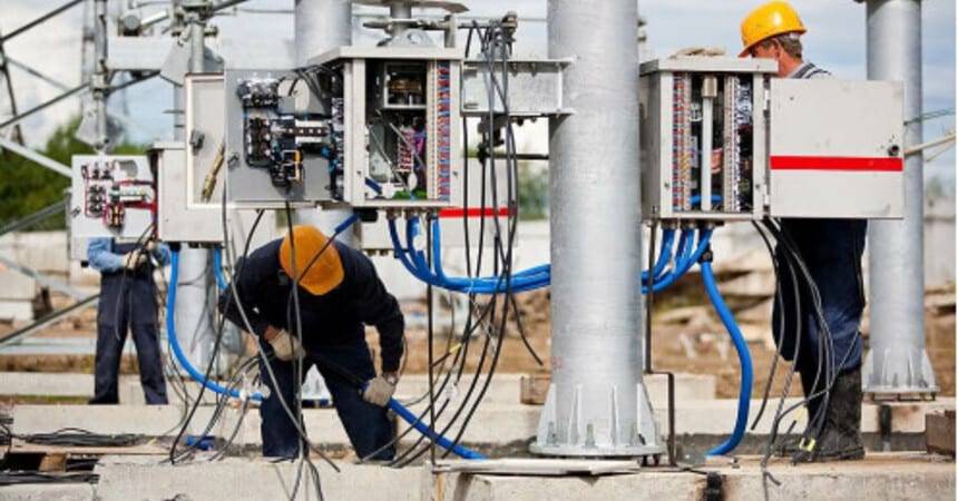 Electricians in hard hats working on switchgear cabinets at an outdoor substation