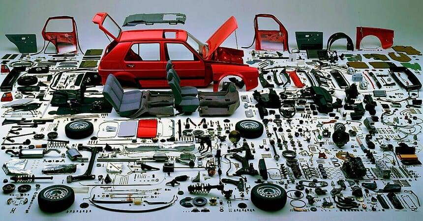 Disassembled red car with every component laid out in rows on a white floor