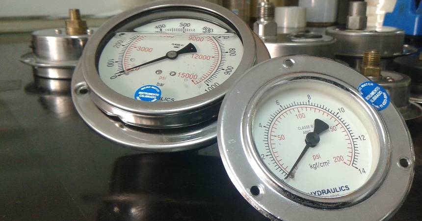 Two stainless steel pressure gauges with white dials resting on a workbench