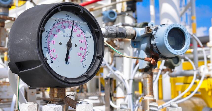 Analogue pressure gauge mounted on a valve manifold with yellow process pipework behind