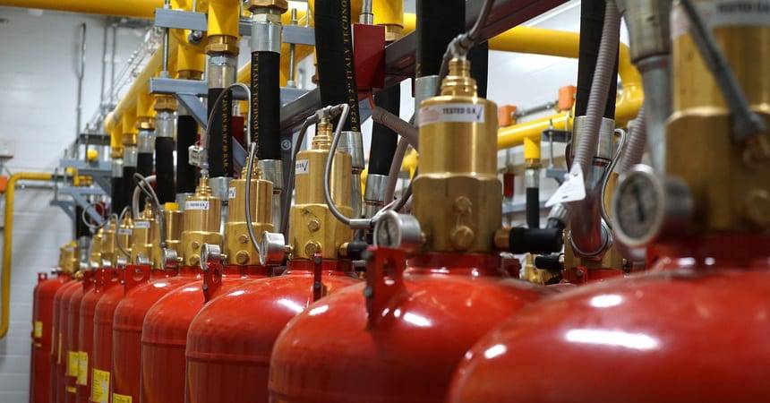 Bank of red gas fire suppression cylinders with brass valves and yellow manifold pipework